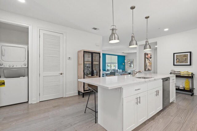 kitchen with a center island with sink, stacked washer / dryer, light hardwood / wood-style floors, white cabinetry, and sink