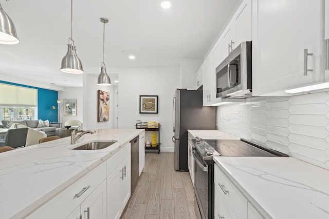 kitchen with appliances with stainless steel finishes, backsplash, sink, white cabinetry, and light hardwood / wood-style flooring