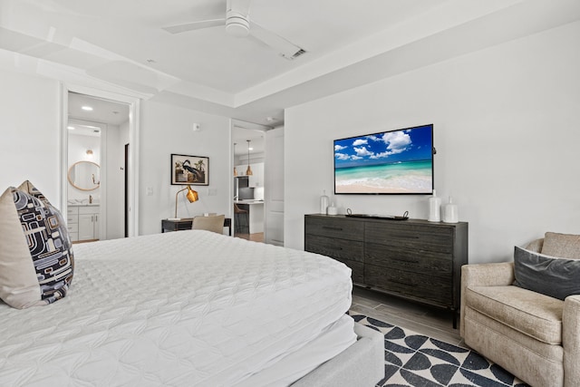 bedroom featuring ensuite bath, light hardwood / wood-style flooring, a tray ceiling, and ceiling fan