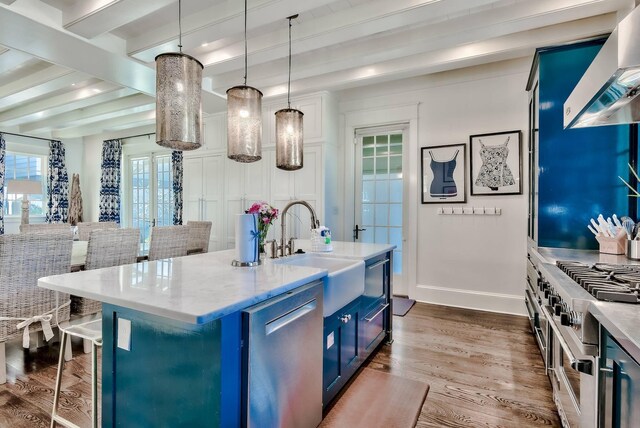 kitchen with wall chimney exhaust hood, blue cabinets, pendant lighting, beam ceiling, and a kitchen island with sink