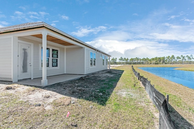 view of property exterior with a patio area, a yard, fence, and a water view