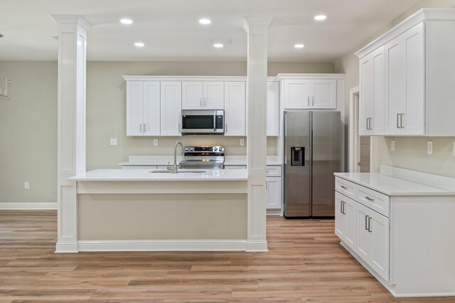 kitchen featuring stainless steel appliances, light hardwood / wood-style flooring, sink, white cabinets, and ornate columns