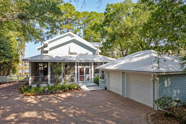 view of front of house with a garage, a sunroom, metal roof, and fence