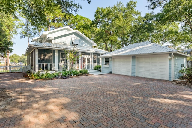 view of front of house featuring a sunroom, a detached garage, fence, and metal roof