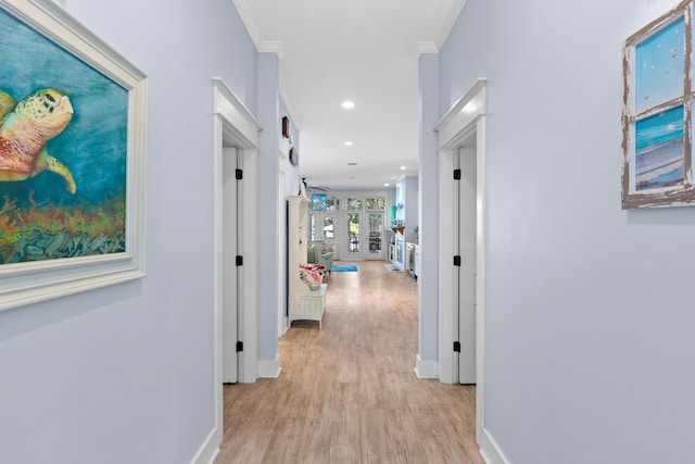 hallway with light wood finished floors, french doors, ornamental molding, and baseboards