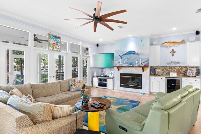 living room featuring wine cooler, light hardwood / wood-style flooring, ceiling fan, crown molding, and a high end fireplace