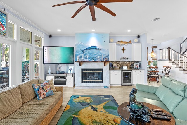 living room featuring light hardwood / wood-style flooring, ornamental molding, wine cooler, a fireplace, and ceiling fan