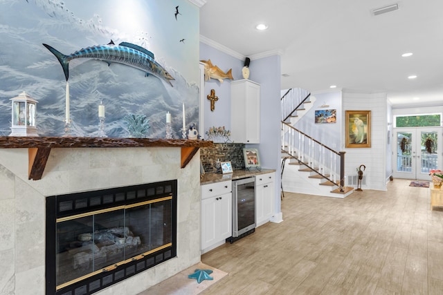 kitchen with light hardwood / wood-style floors, ornamental molding, white cabinets, a tile fireplace, and beverage cooler