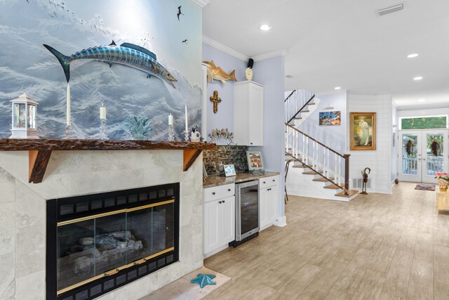 kitchen with white cabinets, light wood-style flooring, wine cooler, ornamental molding, and dark stone countertops