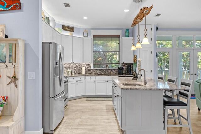 kitchen featuring stainless steel refrigerator with ice dispenser, light stone counters, white cabinets, a kitchen island, and hanging light fixtures