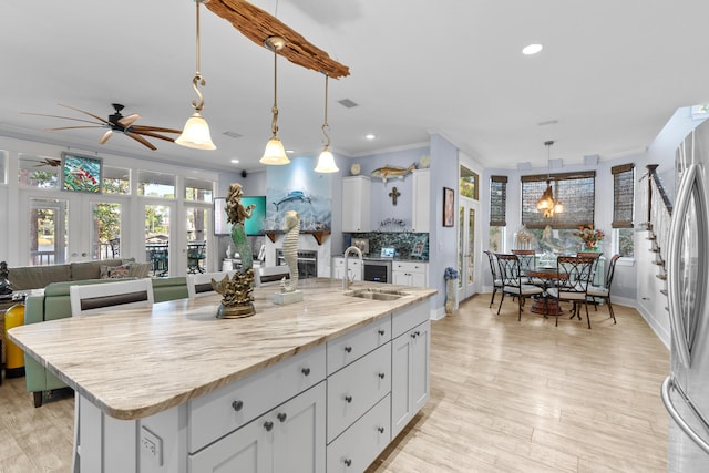 kitchen featuring pendant lighting, a center island with sink, ornamental molding, light stone countertops, and stainless steel refrigerator