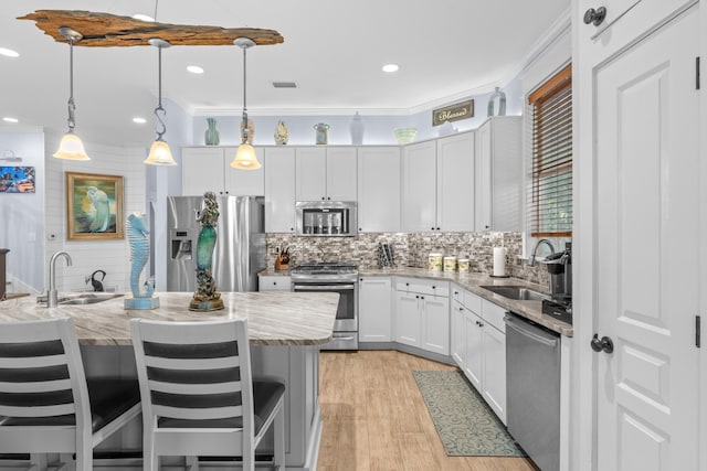 kitchen with light stone counters, stainless steel appliances, a sink, white cabinets, and decorative light fixtures