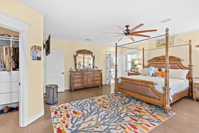 bedroom featuring ceiling fan, ornamental molding, a walk in closet, and wood-type flooring