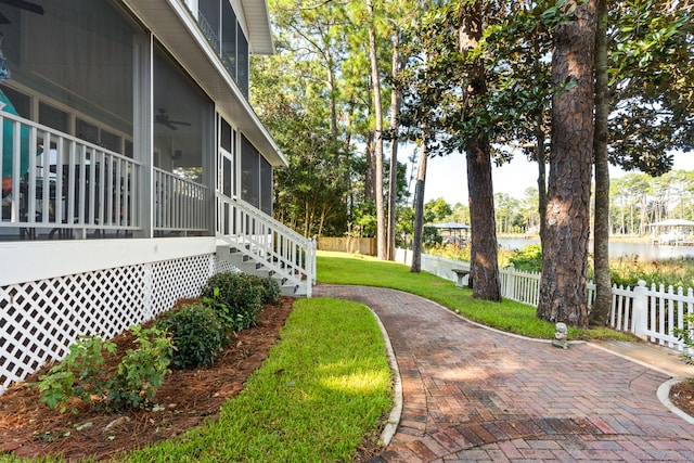 view of yard featuring a water view, stairway, a ceiling fan, a sunroom, and fence