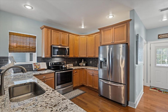 kitchen featuring appliances with stainless steel finishes, hardwood / wood-style flooring, sink, and light stone countertops