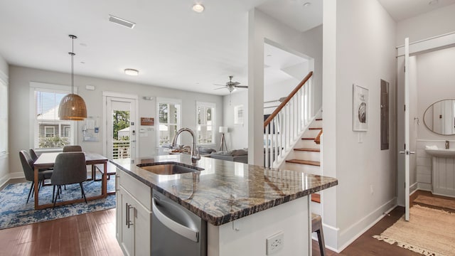 kitchen featuring stainless steel dishwasher, dark hardwood / wood-style floors, sink, dark stone countertops, and hanging light fixtures