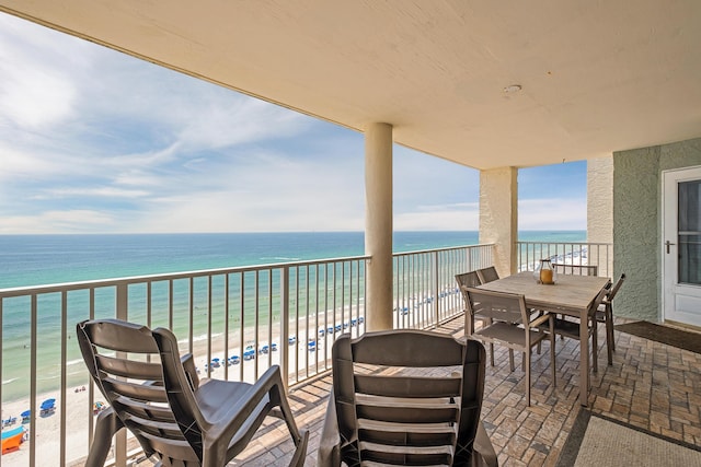 balcony featuring a view of the beach, outdoor dining area, and a water view