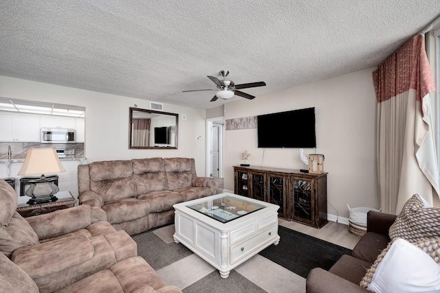 living area with visible vents, light wood-style flooring, a ceiling fan, a textured ceiling, and baseboards