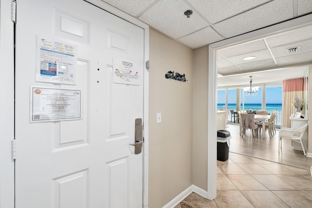 interior space featuring a water view, light tile patterned floors, baseboards, and a drop ceiling