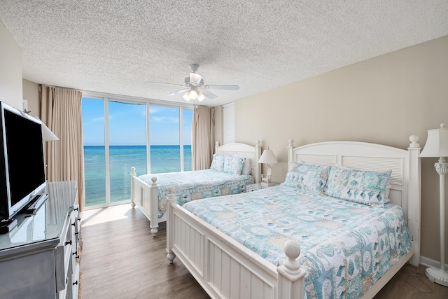 bedroom featuring ceiling fan, wood finished floors, a water view, access to outside, and a wall of windows