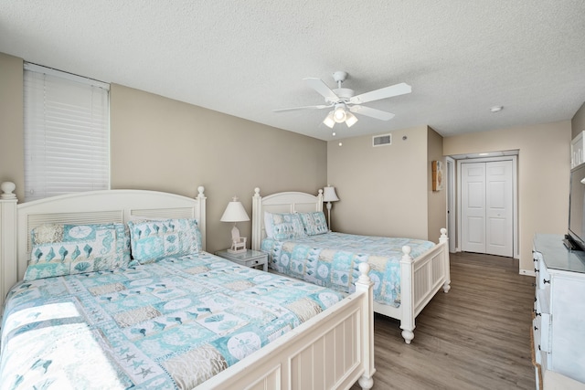 bedroom featuring a ceiling fan, visible vents, a textured ceiling, and wood finished floors