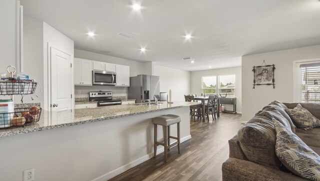 kitchen with stainless steel appliances, white cabinetry, light stone counters, a kitchen breakfast bar, and dark wood-type flooring