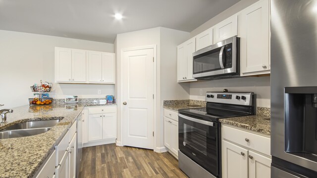 kitchen with appliances with stainless steel finishes, sink, light stone counters, white cabinets, and hardwood / wood-style flooring