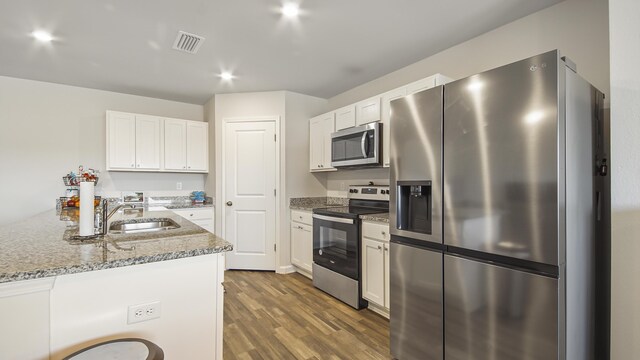 kitchen with hardwood / wood-style floors, white cabinets, appliances with stainless steel finishes, light stone counters, and sink