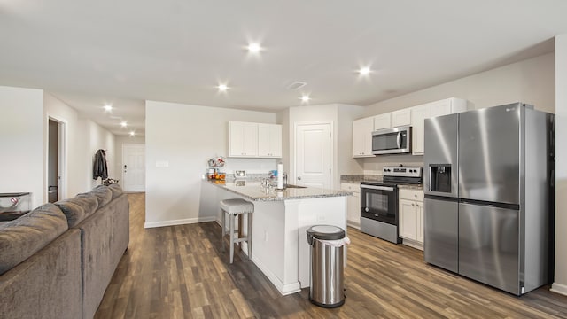 kitchen featuring stainless steel appliances, dark wood-type flooring, white cabinetry, and a kitchen bar