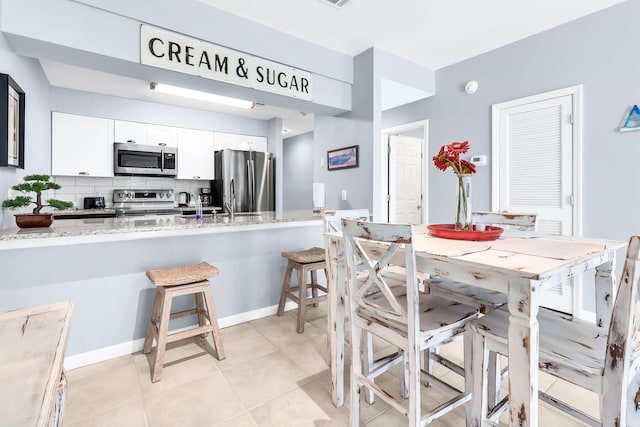 kitchen with stainless steel appliances, light stone countertops, backsplash, white cabinets, and a breakfast bar area