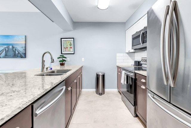 kitchen featuring appliances with stainless steel finishes, dark brown cabinets, light stone counters, light tile patterned floors, and sink