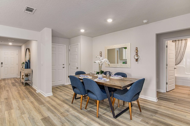 dining space with a textured ceiling and light hardwood / wood-style flooring