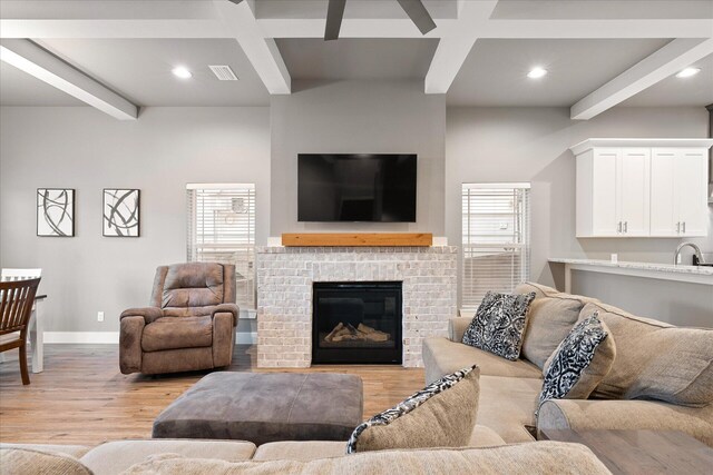 living room with coffered ceiling, beamed ceiling, sink, a brick fireplace, and light wood-type flooring