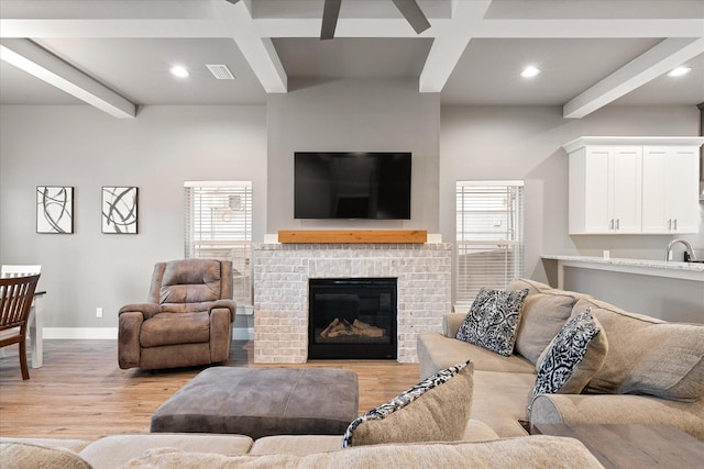 living room featuring beam ceiling, a fireplace, light wood-style flooring, and baseboards