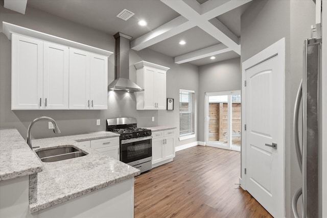 kitchen featuring appliances with stainless steel finishes, white cabinets, a sink, and wall chimney range hood