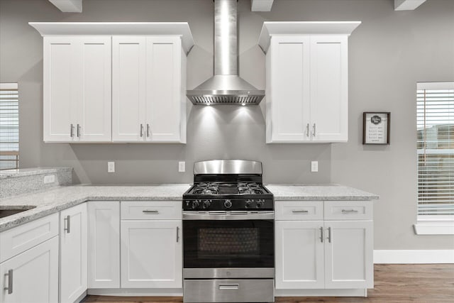 kitchen featuring stainless steel gas range, wall chimney exhaust hood, white cabinetry, and light hardwood / wood-style flooring