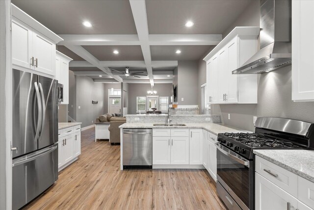 kitchen featuring coffered ceiling, light hardwood / wood-style flooring, ceiling fan, wall chimney exhaust hood, and appliances with stainless steel finishes