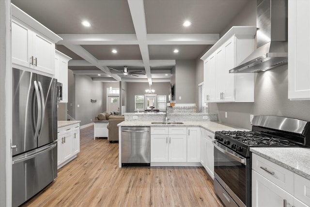 kitchen with stainless steel appliances, open floor plan, white cabinets, a sink, and wall chimney range hood