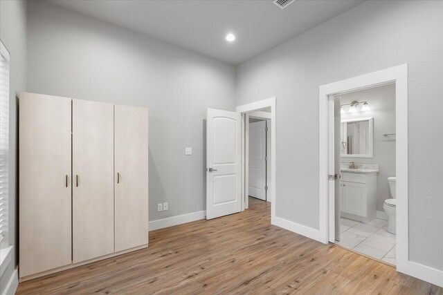 unfurnished bedroom with ensuite bath, light wood-type flooring, a sink, and baseboards