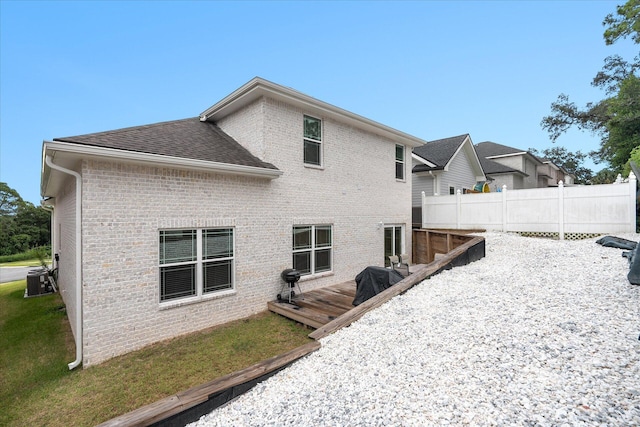 rear view of house with central AC, brick siding, fence, roof with shingles, and a wooden deck