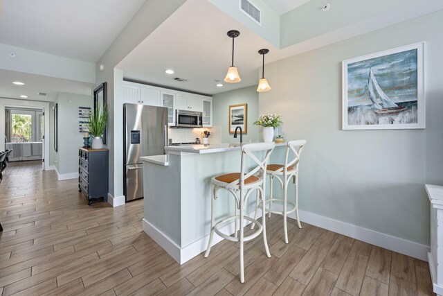 kitchen with white cabinets, kitchen peninsula, decorative light fixtures, appliances with stainless steel finishes, and a breakfast bar