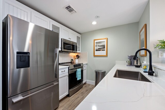 kitchen featuring light stone counters, light hardwood / wood-style floors, sink, white cabinetry, and appliances with stainless steel finishes