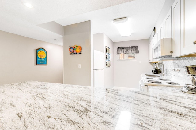 kitchen with white appliances, light stone counters, a textured ceiling, white cabinets, and decorative backsplash