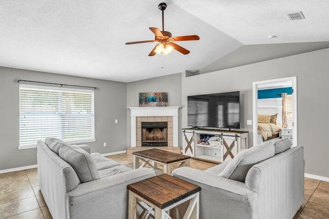 tiled living room featuring vaulted ceiling, ceiling fan, a fireplace, and a textured ceiling