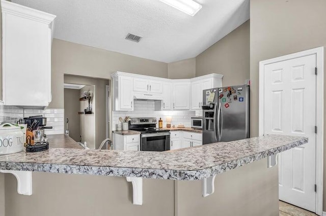 kitchen with appliances with stainless steel finishes, a kitchen bar, white cabinets, and kitchen peninsula