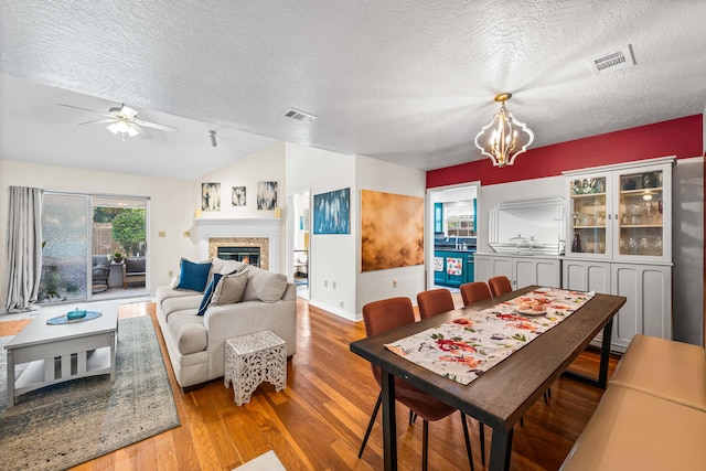 dining space featuring light wood-type flooring, ceiling fan with notable chandelier, a textured ceiling, and lofted ceiling