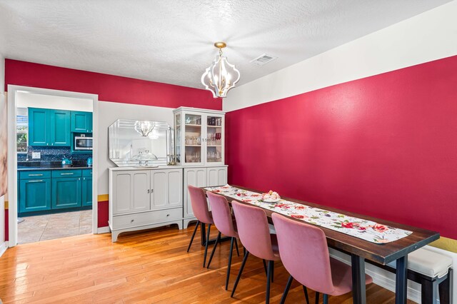 dining room with light hardwood / wood-style floors, an inviting chandelier, and a textured ceiling