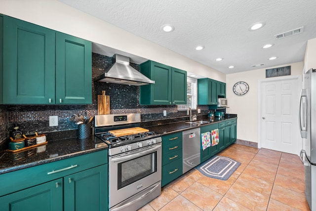 kitchen with appliances with stainless steel finishes, wall chimney exhaust hood, tasteful backsplash, green cabinetry, and dark stone counters