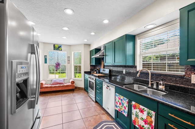 kitchen featuring appliances with stainless steel finishes, backsplash, wall chimney exhaust hood, sink, and light tile patterned floors