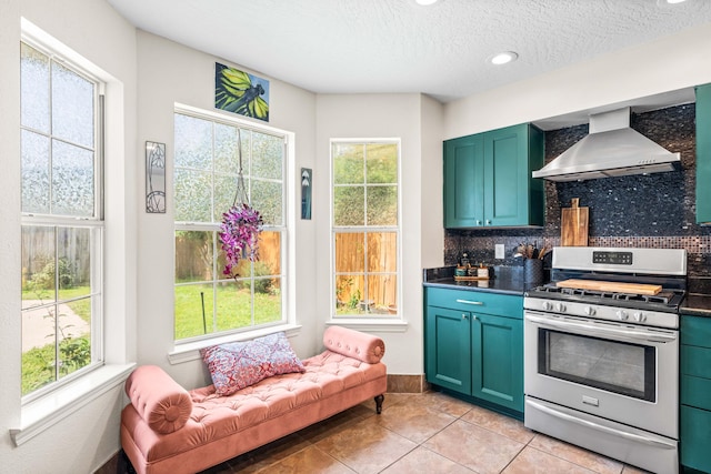 kitchen with wall chimney range hood, stainless steel range with gas stovetop, a healthy amount of sunlight, and light tile patterned floors